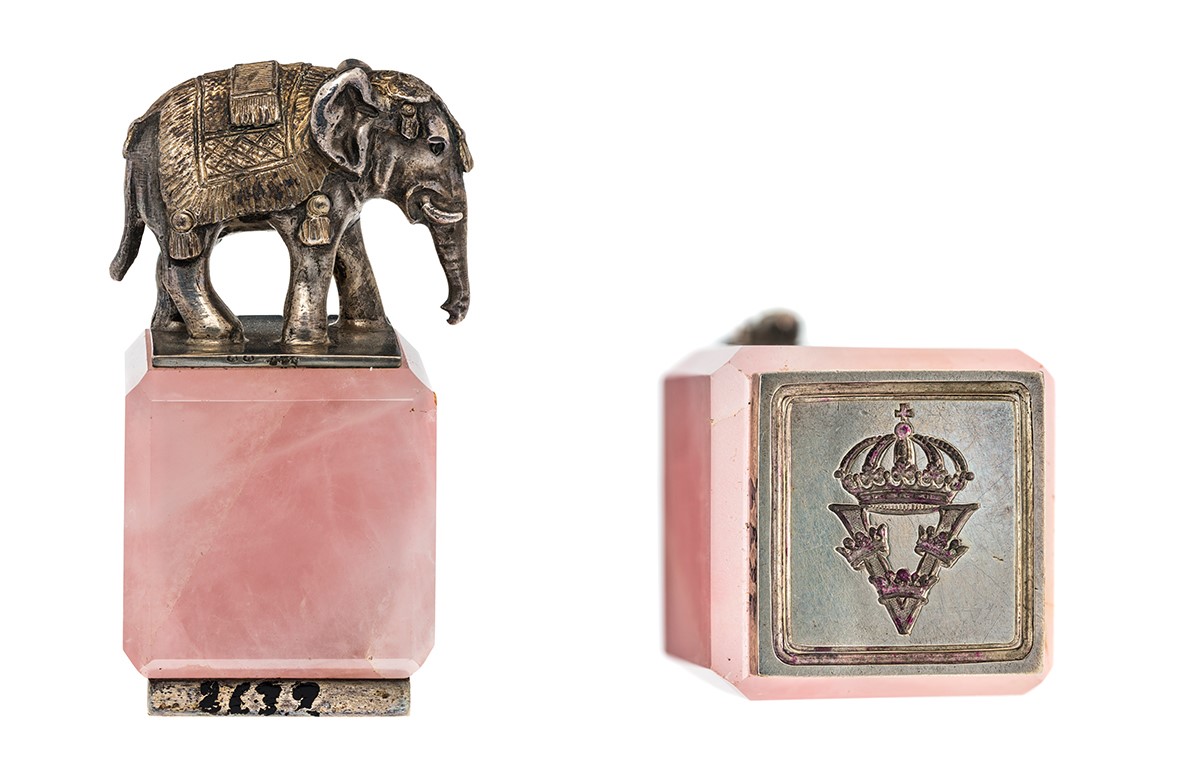 En liten elefant staty som står på en rosa kvadratisk sten.