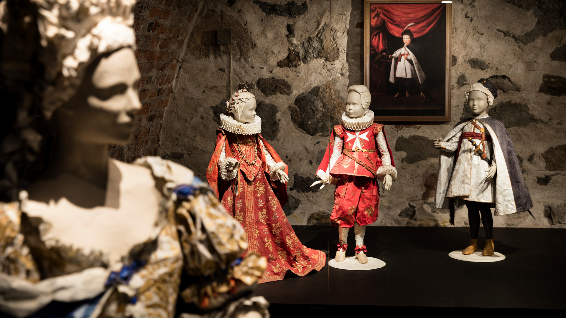 En docka i förgrunden i klänning och i bakgrunden är tre mindre skyltdockor som ska se ut som barn som bär pappersdräkter