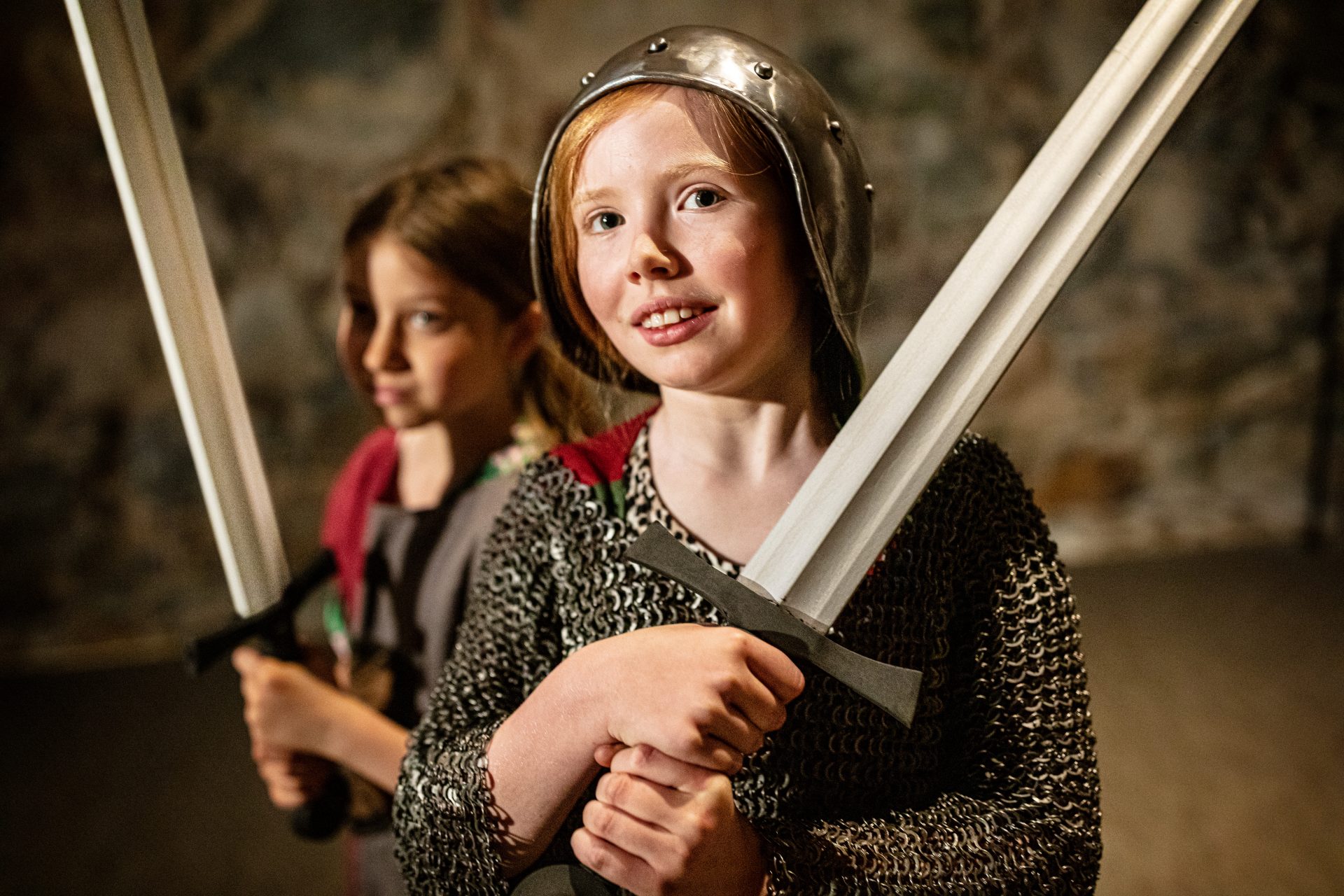 Two children dressed in separate suits of armor, each holding a toy sword.