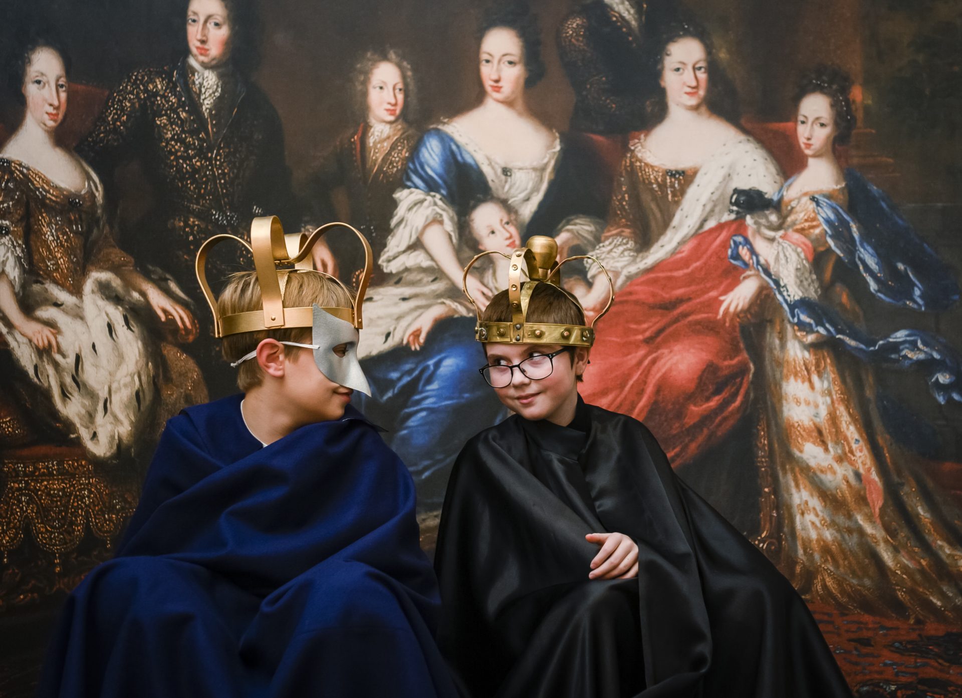 Two children are playing with crowns, masks, and costumes.