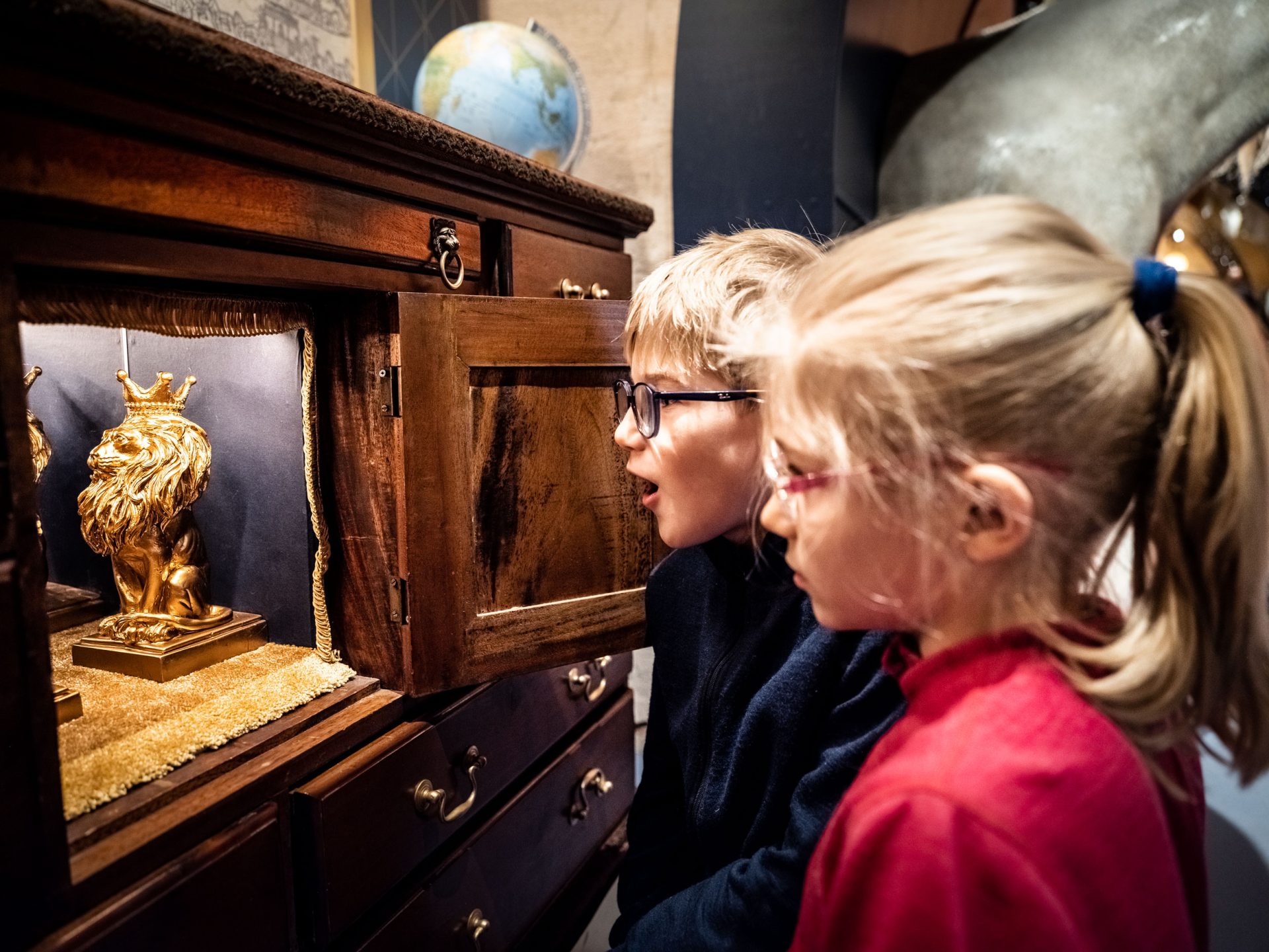 Två barn som tittar in på två guldlejon som står i ett skåp.