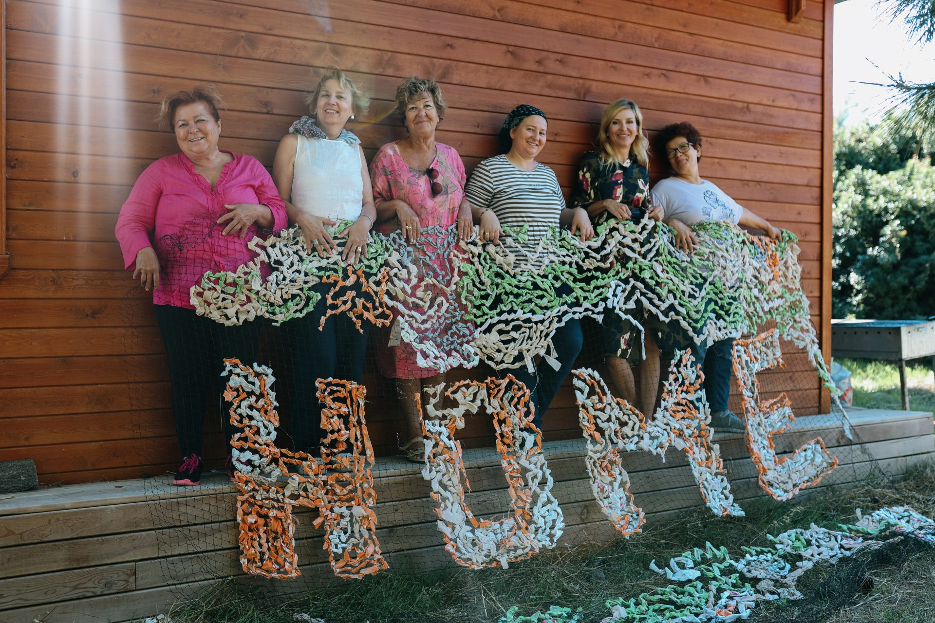 Six artists holding a camouflage net that says Home.