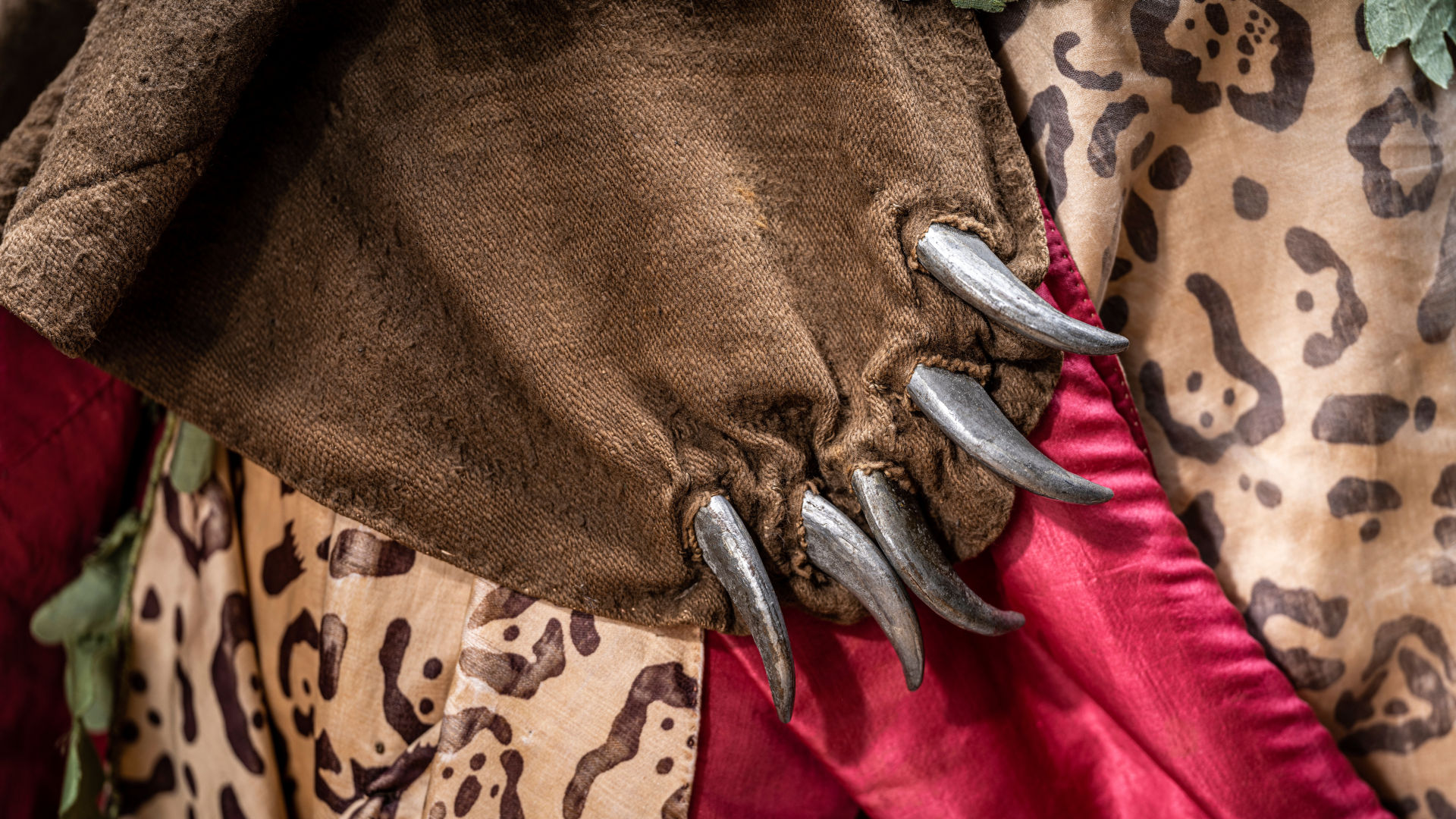 A detail from a costume in silk with a painted leopard pattern. The costume features claws meant to resemble bear fur.