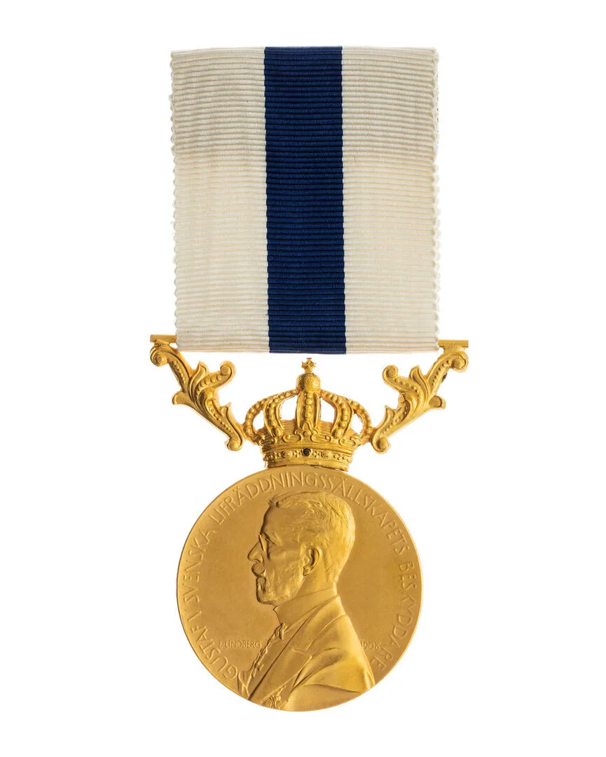 Rund guldmedalj med porträtt av Gustaf V. Bilden på kungen är en bröstbild i profil vänster. Där kungen är klädd i frack och så står en ordnar signatur till vänster.