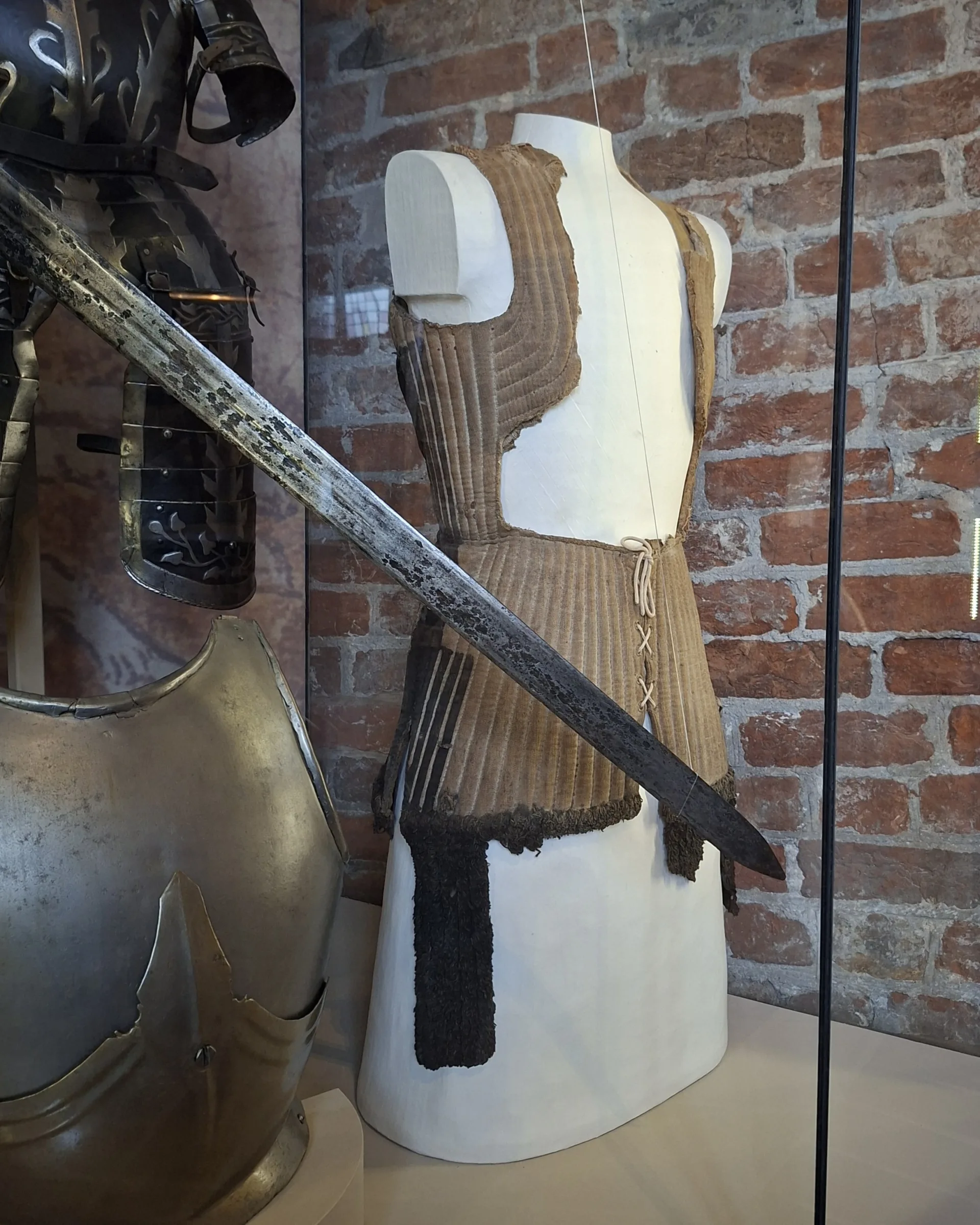 En beige rock på en vit docka. Vid sidan av dockan hänger en rustning och ett svärd.